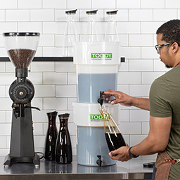 Barista dispensing cold brew from stacked commercial models into decanter